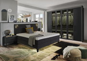 Moderne Schlafzimmeransicht mit einem großen, sechstürigen Drehtürenschrank in dunklem Design, neben einem stilvollen Bett mit gepolstertem Kopfteil. Perspektive von der Seite des Bettes.