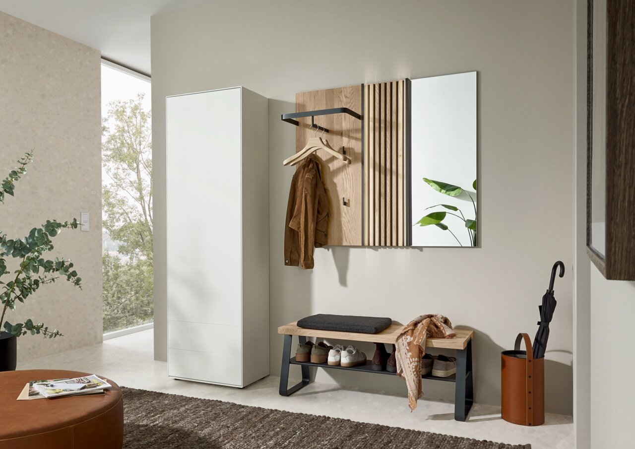 Moderne Garderobenkombination mit weißem Schrank, hölzerner Wandgarderobe, Spiegel und Sitzbank mit Kissen, seitliche Perspektive.