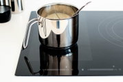 Edelstahl-Kochtopf mit Milch und Rührlöffel auf schwarzem Induktionskochfeld, schräg von vorne aus leicht erhöhter Perspektive aufgenommen