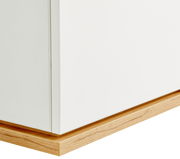 Nahaufnahme einer weißen Kommode mit Holzsockel, seitliche Perspektive.