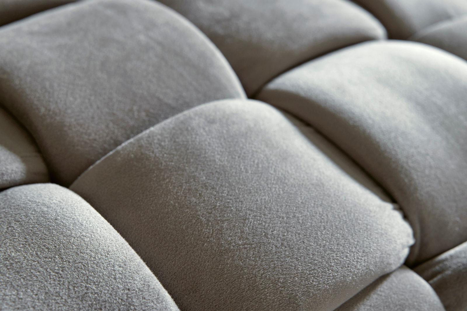 Nahaufnahme eines gepolsterten Hockers mit weicher, grauer Oberfläche in quadratischem Muster.