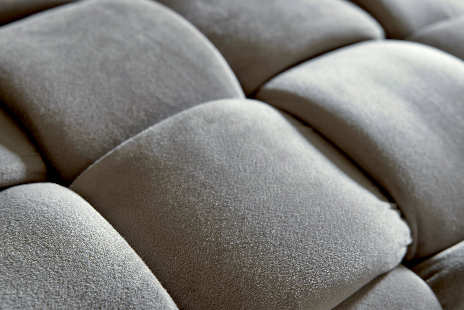 Nahaufnahme eines gepolsterten Hockers mit weicher, grauer Oberfläche in quadratischem Muster.