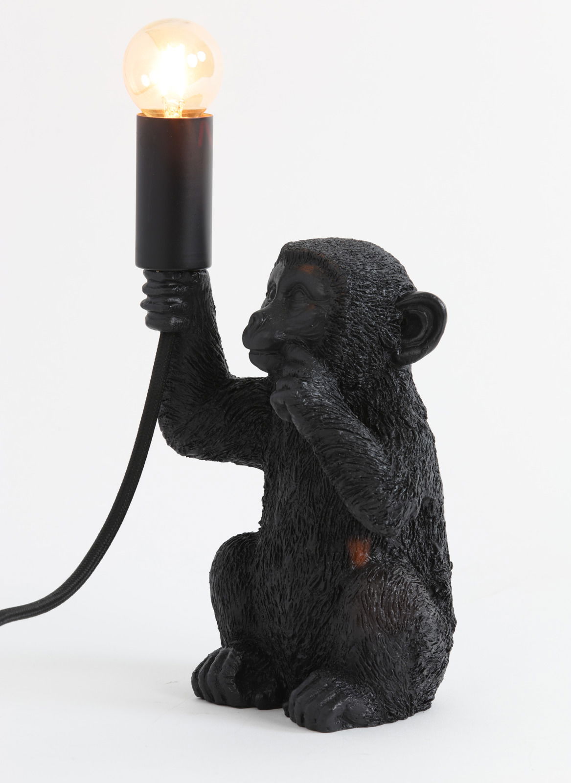 Schwarze Tischleuchte in Form eines Affen, der eine Glühbirne in der Hand hält. Seitenansicht.