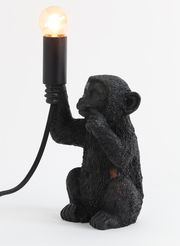 Schwarze Tischleuchte in Form eines Affen, der eine Glühbirne in der Hand hält. Seitenansicht.