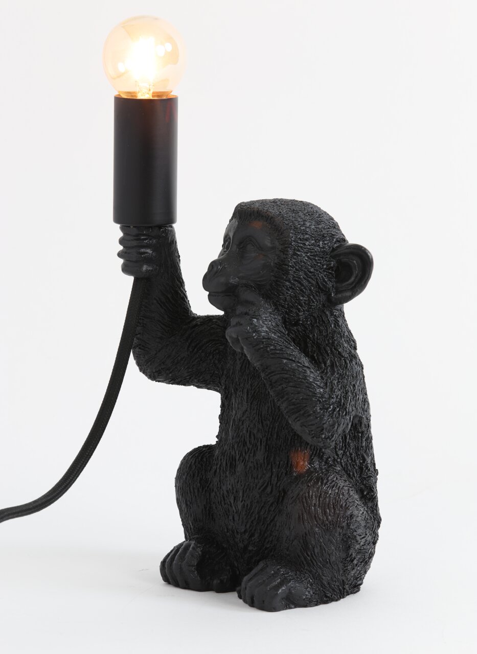 Zwarte tafellamp in de vorm van een aap die een gloeilamp in zijn hand houdt. Zijaanzicht.