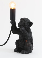 Schwarze Tischleuchte in Form eines Affen, der eine Glühbirne in der Hand hält. Seitenansicht.