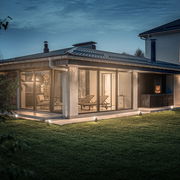 Moderne Terrasse mit Glaswänden und gemütlichen Liegestühlen, beleuchtet von Bodenspikes in der Abenddämmerung, seitliche Perspektive.