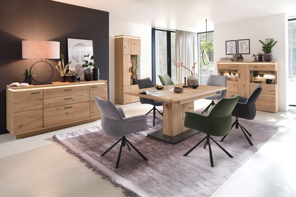 Wohnzimmer mit modernem Esstisch-Set aus Holz, bestehend aus einem Esstisch, sechs Stühlen in Grau und Grün, einem Sideboard, einer Vitrine und einem Wandboard. Perspektive: Frontalansicht des gesamten Sets in einem hellen Raum mit großen Fenstern.
