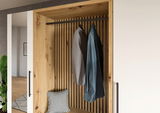 Kompaktgarderobe aus Holz mit zwei aufgehängten Hemden und einem Kissen, frontal betrachtet.