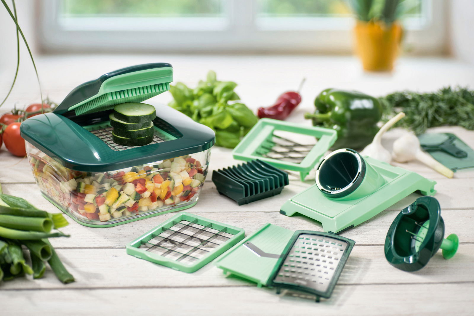 Nicer Dicer Chef 15-teiliges Set in einer Küchenumgebung, mit verschiedenen Schneideinsätzen und einem Behälter voller geschnittener Gemüsewürfel, aus der Perspektive von vorne.