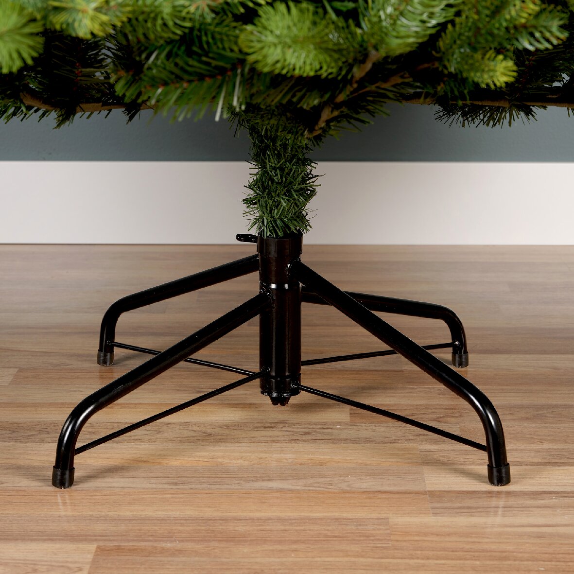 Close-up van een stevige zwarte metalen standaard voor een kunstkerstboom op een houten vloer, gezien vanaf de zijkant.