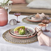 Elegante Tischdekoration mit Sekt- und Dessertschalen in Rosa, gedeckt mit Salat und Besteck, aus seitlicher Perspektive.