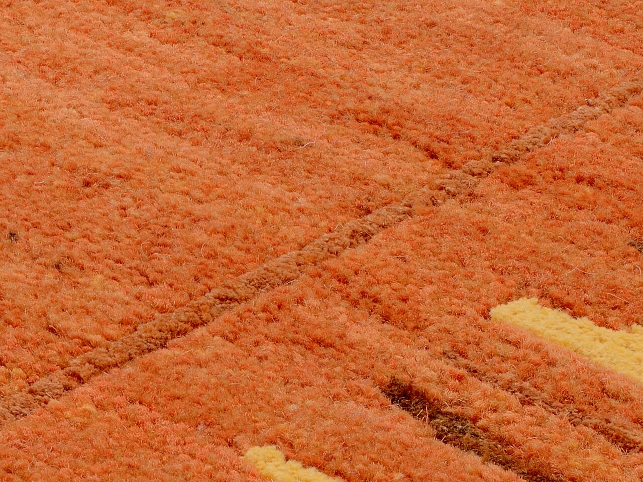 Nahaufnahme eines orangefarbenen Wollteppichs mit gelben Akzenten, aus einer schrägen Perspektive fotografiert.
