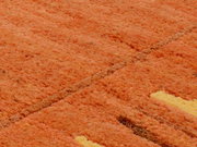 Nahaufnahme eines orangefarbenen Wollteppichs mit gelben Akzenten, aus einer schrägen Perspektive fotografiert.
