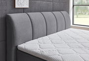 Seitliche Ansicht eines grauen Boxspringbetts mit gepolstertem Kopfteil und weißer Matratze in einem modernen Schlafzimmer.