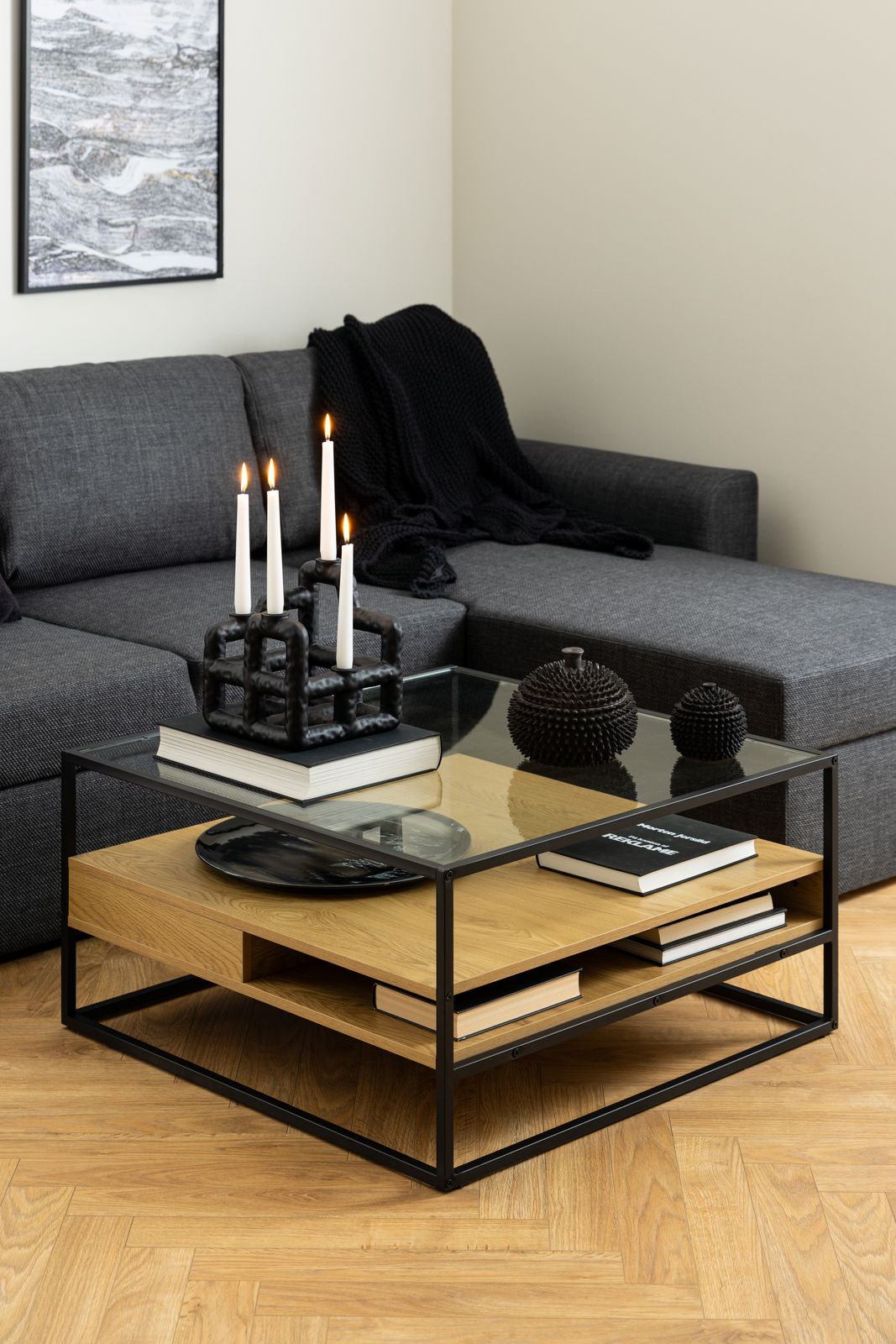 Moderner Couchtisch mit Glasplatte und Holzablage, dekoriert mit Kerzen und Büchern, aus seitlicher Perspektive fotografiert.
