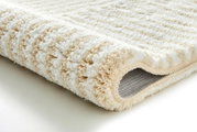 Nahaufnahme eines beigen und weißen Badteppichs, der aufgerollt ist und die weiche, flauschige Textur zeigt.