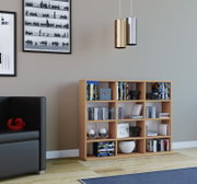 Modernes Holzregal mit vielen Fächern, gefüllt mit DVDs, Büchern und Deko, in einem Wohnzimmer; Ansicht aus frontaler Perspektive leicht von links, mit Sofa links und zwei zylindrischen Pendelleuchten oben rechts.