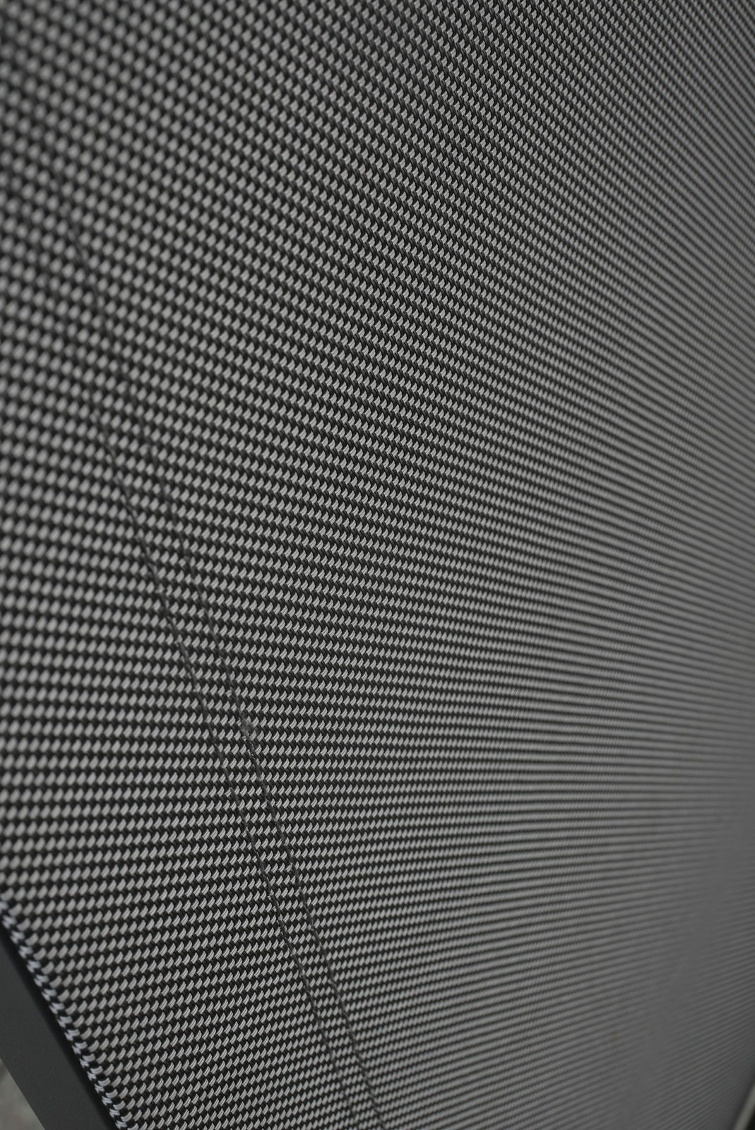 Nahaufnahme eines Stapelstuhls mit schwarzem, gewebtem Stoffbezug, von der Seite betrachtet.