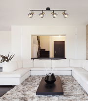 Deckenstrahler aus Metall in Schwarz mit vier verstellbaren Leuchten, perspektivisch von unten in einem modernen Wohnzimmer mit weißem Sofa und Teppich.