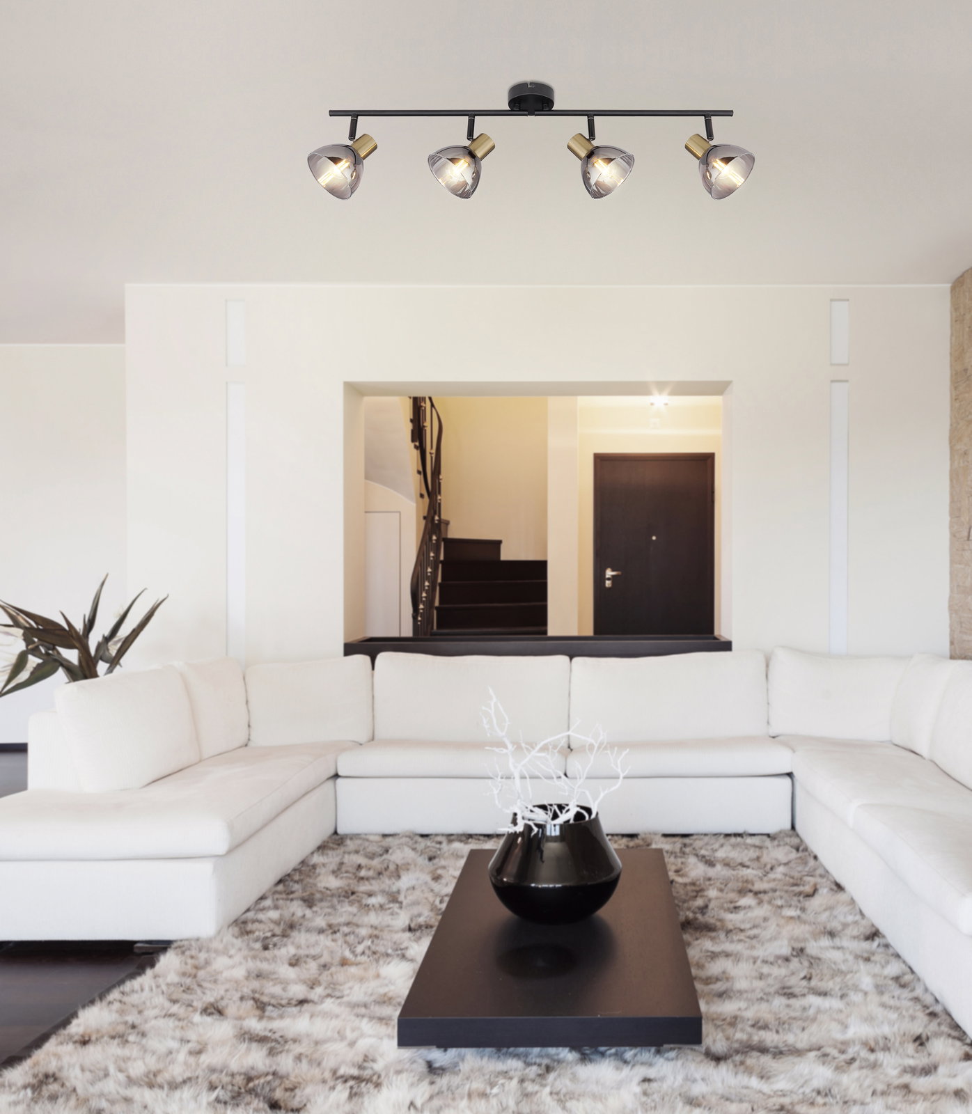 Deckenstrahler aus Metall in Schwarz mit vier verstellbaren Leuchten, perspektivisch von unten in einem modernen Wohnzimmer mit weißem Sofa und Teppich.