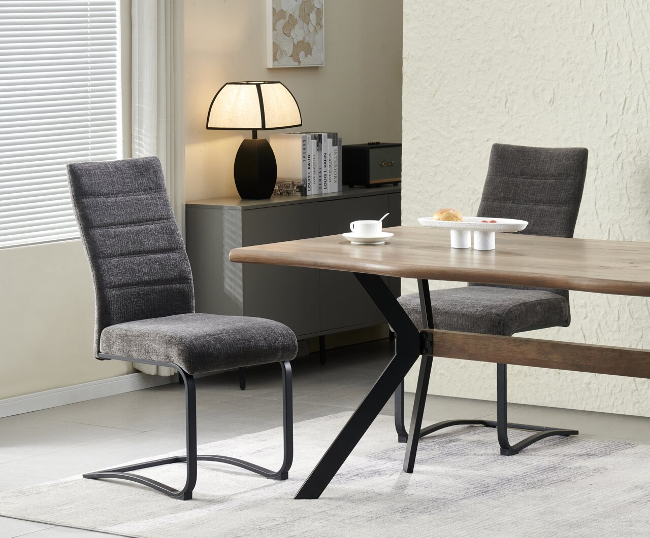 MID.YOU Schwingstuhl 2er-Set TINA Modernes Esszimmer-Set mit rechteckigem Holztisch und schwarzen Metallbeinen sowie zwei grauen Polster-Schwingstühlen, fotografiert in schräger Seitenansicht im Wohnambiente.