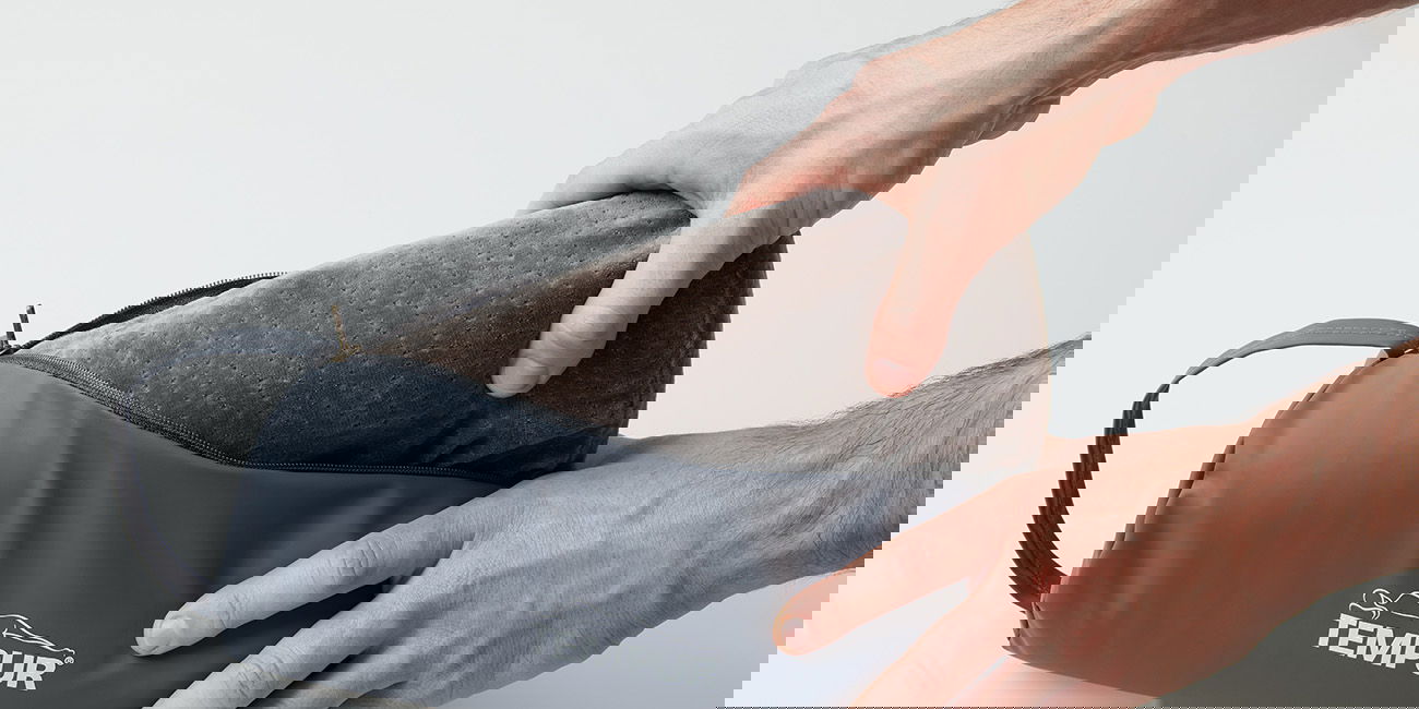 Hände verstauen ein Reisekissen in einer grauen Tasche mit Tempur-Logo.