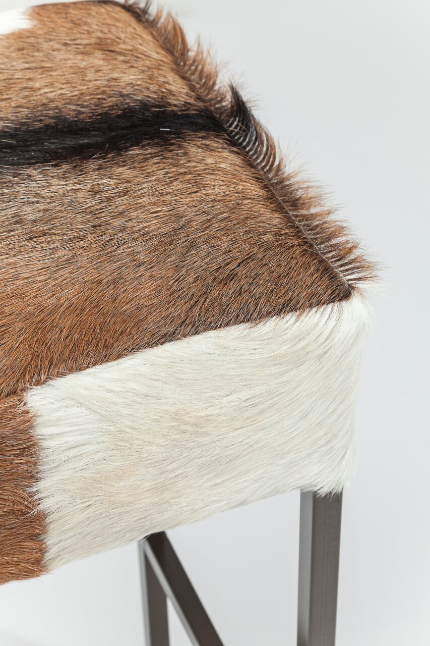 Nahaufnahme eines Hockers mit Fellbezug in Braun- und Weißtönen, seitliche Perspektive