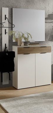 Modernes weißes Sideboard/Schuhschrank mit zwei Türen und Schublade mit Holzlamellenfront, davor frontal leicht schräg fotografiert, mit Spiegel darüber und Garderobenleiste an Betonwand