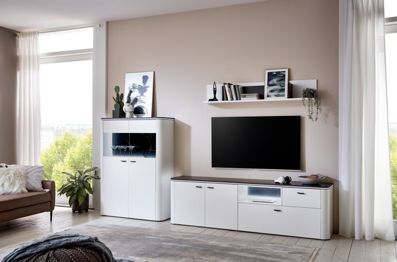 Zurbrüggen Wandcombinatie WAVE Moderne weiße Wandkombination mit TV-Schrank, Regal und Vitrine in einem hellen Wohnzimmer, seitliche Perspektive.