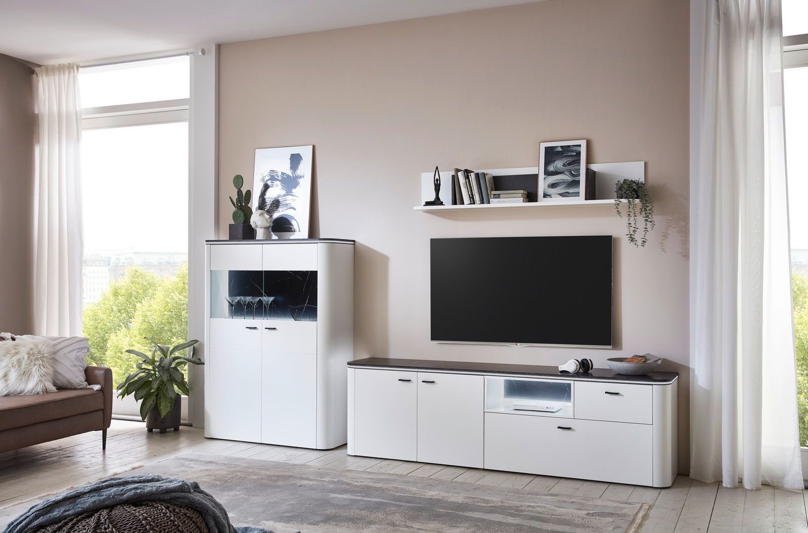 Moderne weiße Wandkombination mit TV-Schrank, Regal und Vitrine in einem hellen Wohnzimmer, seitliche Perspektive.