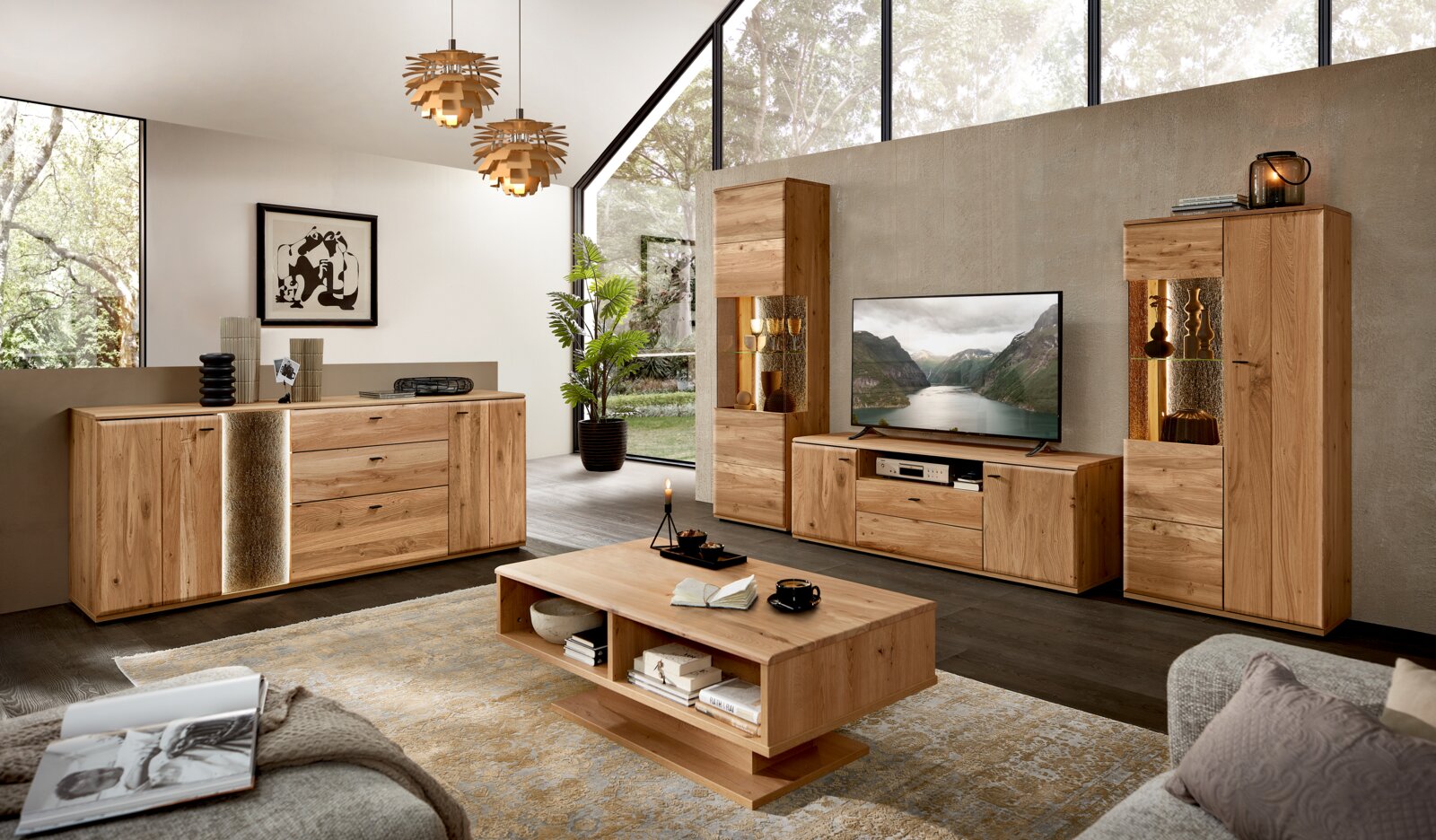 Moderne woonkamer met massief houten meubelset in eikenlook: dressoir, tv-meubel met tv, twee vitrinekasten met sfeerverlichting en salontafel op een vloerkleed, gefotografeerd in frontaal breedbeeldperspectief.