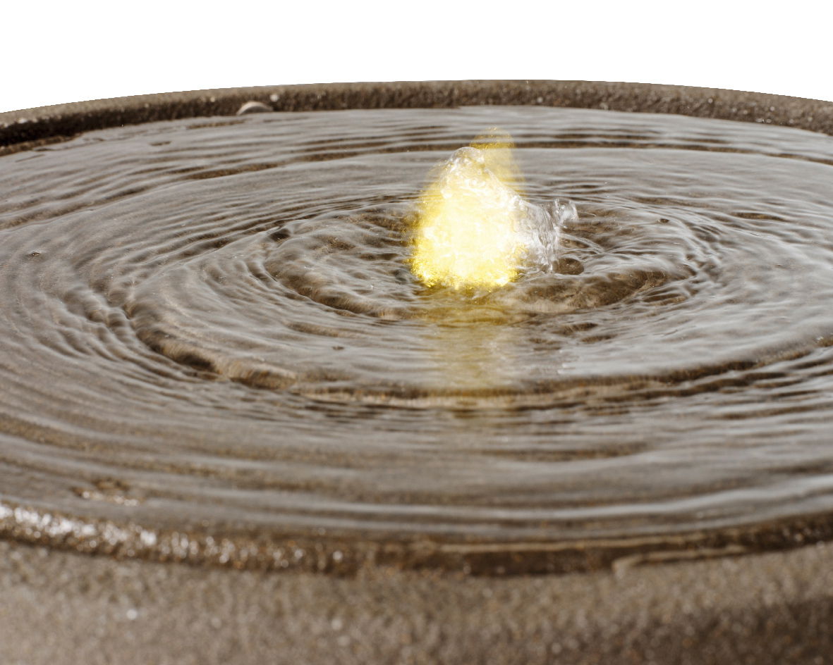 Nahaufnahme eines Brunnens mit sprudelndem Wasser und gelbem Licht in der Mitte, von oben betrachtet.