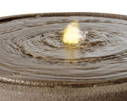 Nahaufnahme eines Brunnens mit sprudelndem Wasser und gelbem Licht in der Mitte, von oben betrachtet.