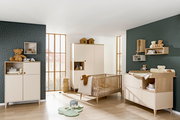 Kinderzimmer mit Babybett, Wickelkommode und Kleiderschrank in heller Holzoptik, seitliche Perspektive