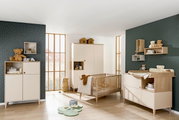 Kinderzimmer mit Babybett, Wickelkommode und Kleiderschrank in heller Holzoptik, seitliche Perspektive