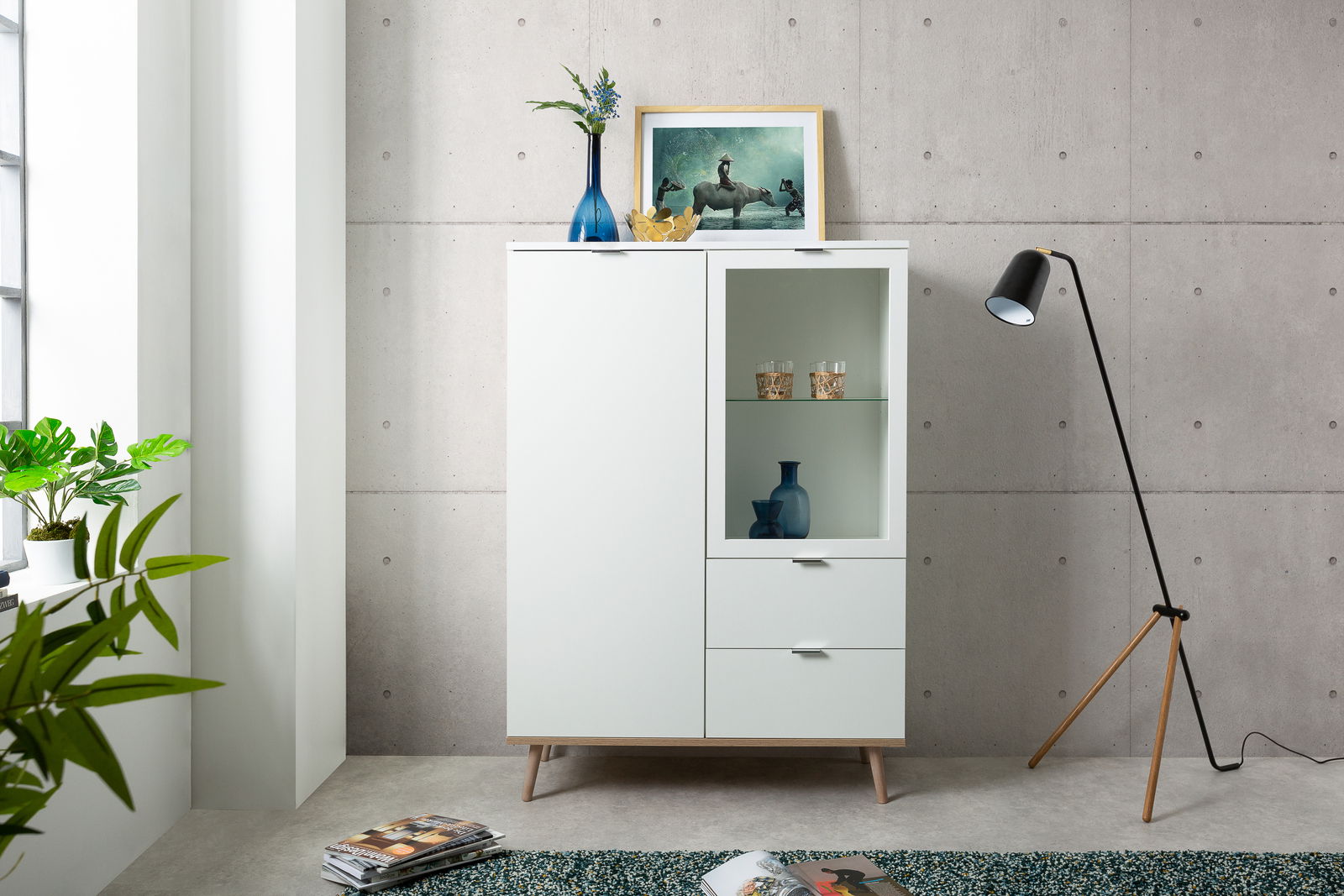Modernes Highboard in Weiß mit Glasvitrine, dekoriert mit Vasen und einem Bild, seitliche Perspektive