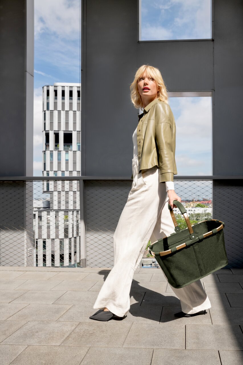 Frau in eleganter Kleidung trägt eine grüne Tragetasche, seitliche Perspektive, im urbanen Umfeld.