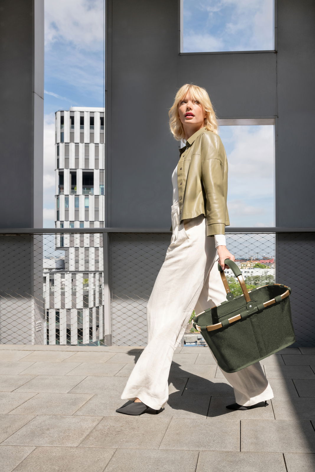 Frau in eleganter Kleidung trägt eine grüne Tragetasche, seitliche Perspektive, im urbanen Umfeld.
