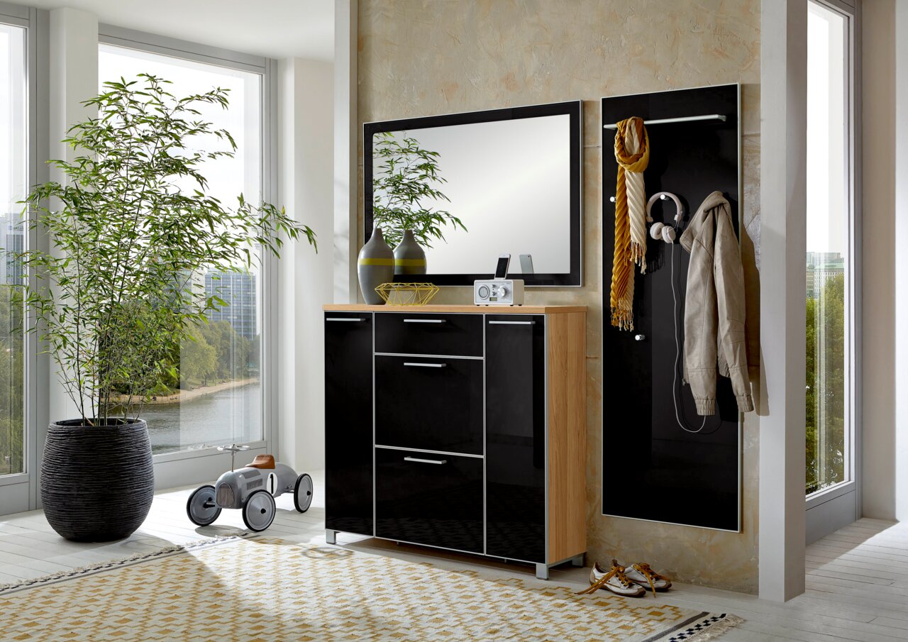 Modernes Garderoben-Set in einem hellen Raum mit großen Fenstern, bestehend aus einem schwarzen Schrank mit Holzdetails, einem Spiegel und einer Wandpaneele mit Haken. Perspektive von vorne.