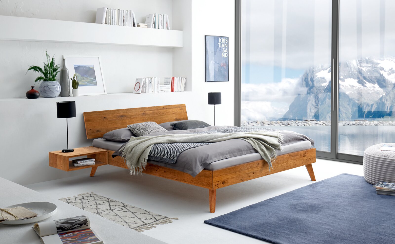 Modernes Bettgestell aus Holz in einem hellen, stilvollen Schlafzimmer mit Blick auf eine verschneite Berglandschaft durch große Fenster, seitliche Perspektive.