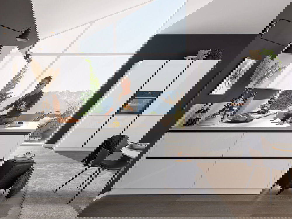 Helle Küche in L-Form mit Holz- und Weißtönen, eine Frau räumt die Spülmaschine aus und ein Hund liegt daneben.