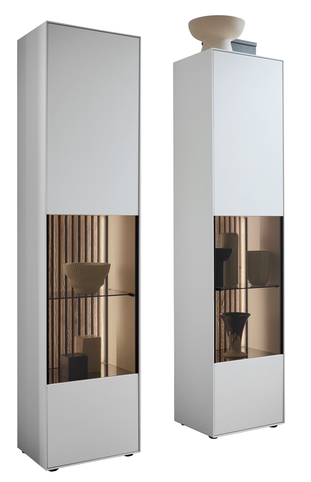 Zwei moderne Vitrinen in Weiß mit Glaseinsätzen, die von vorne gezeigt werden. Die linke Vitrine enthält dekorative Objekte wie Schalen und Vasen.