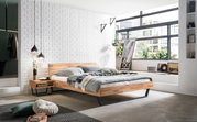 Modernes Schlafzimmer mit einem stilvollen Bettgestell aus Holz und Metall, seitliche Perspektive. Das Zimmer ist hell und minimalistisch eingerichtet mit großen Fenstern und dekorativen Elementen.