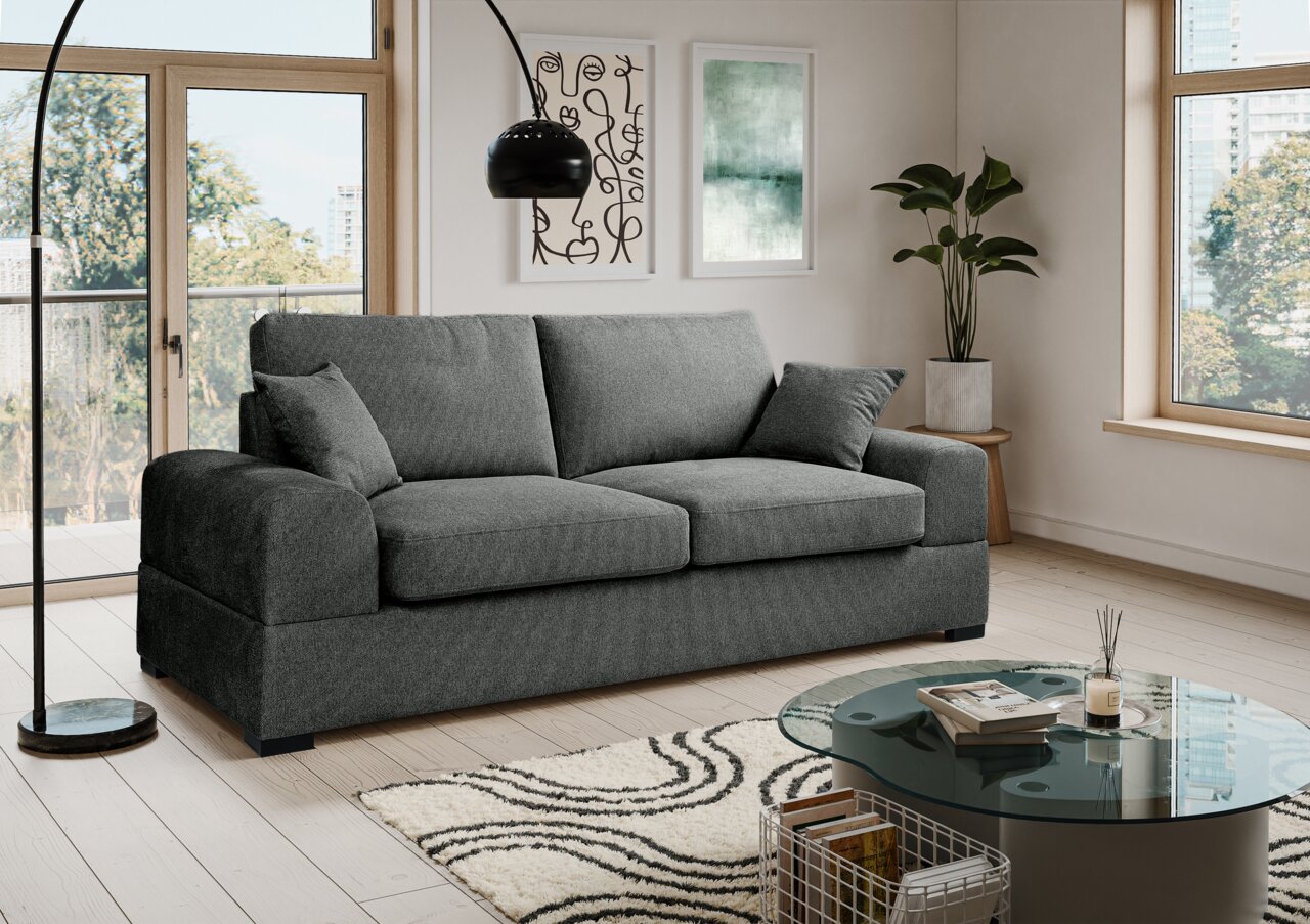 MID.YOU 3-Sitzer VEDA Modernes graues 3-Sitzer-Stoffsofa mit breiten Armlehnen und zwei Kissen im hellen Wohnzimmer, Frontansicht leicht schräg von links