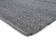 Grauer Handweb Teppich in Nahaufnahme, perspektivisch von der Seite fotografiert.