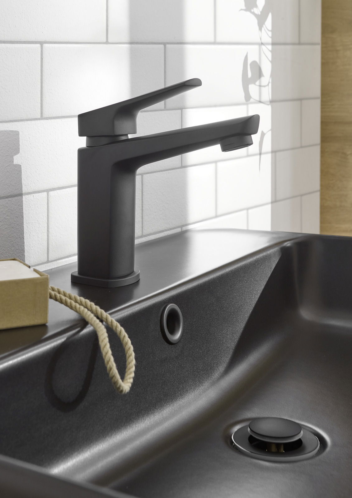 Moderne schwarze Waschtischarmatur in seitlicher Perspektive, montiert auf einem dunklen Waschbecken vor einer weißen Fliesenwand.