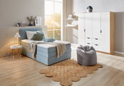 Gemütliches Boxspringbett in einem modernen Schlafzimmer mit Tageslicht, aus der Seitenperspektive fotografiert.