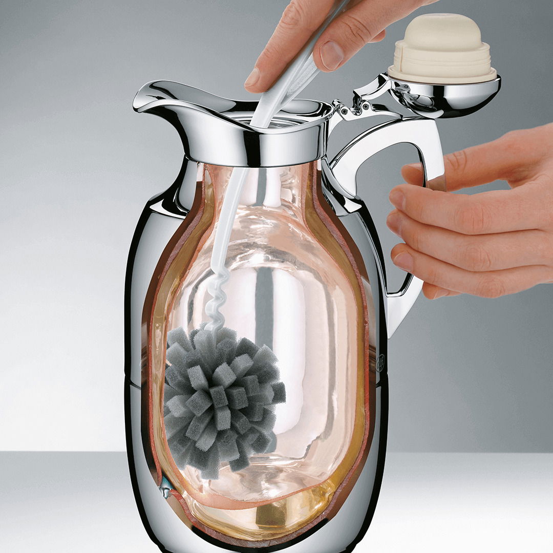 Nahaufnahme einer Kanne mit einem Reinigungsgerät im Inneren, das von einer Hand bedient wird.