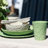 Ein Set aus einem tiefen Teller, einer Schüssel und einem Becher in grünem und weißem geometrischem Design, auf einem Tisch im Freien von der Seite fotografiert.